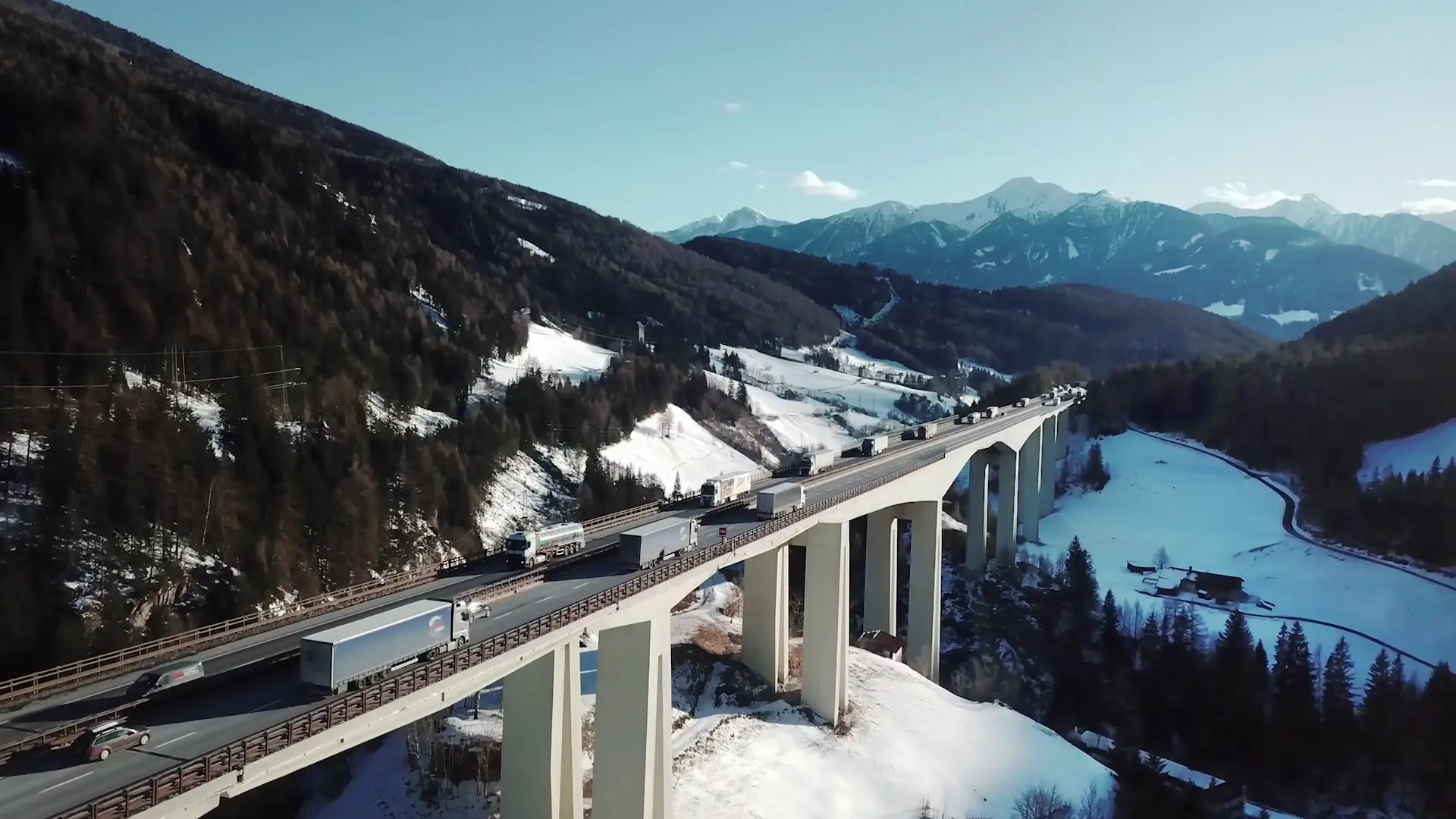 Viadotto autostradale innevato tra le montagne, con un camion in transito