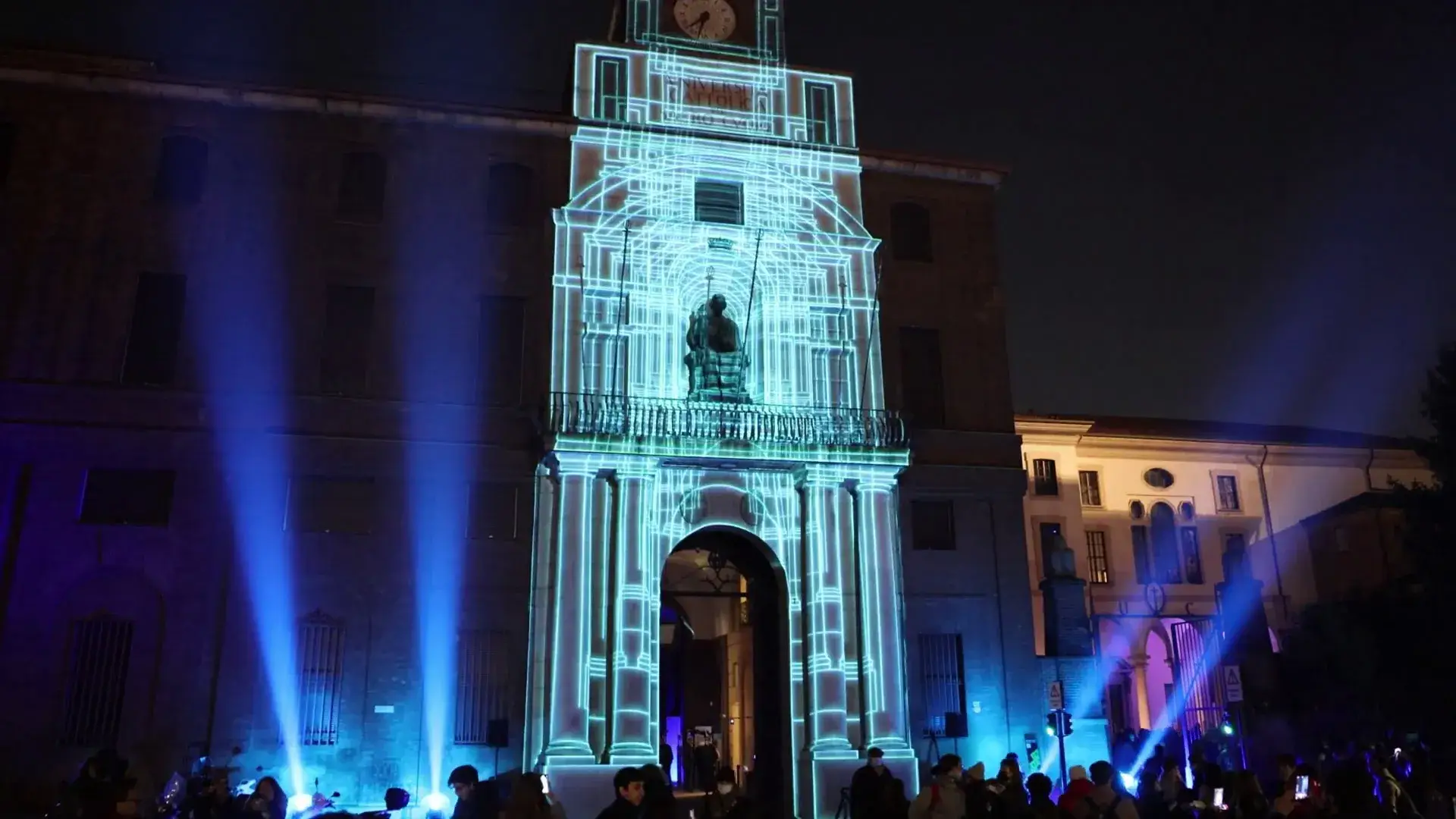 Torre dell’università illuminata da un video mapping azzurro, con il pubblico in piazza