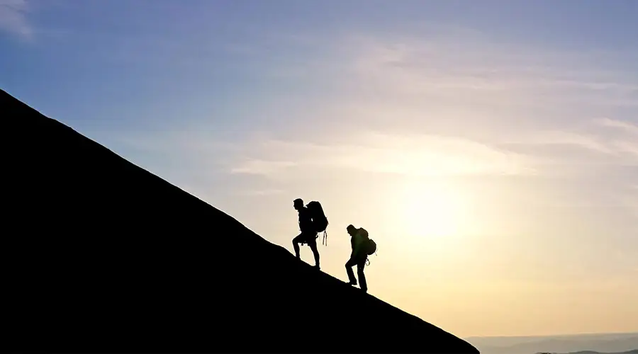 Due alpinisti in controluce risalgono un pendio all’alba