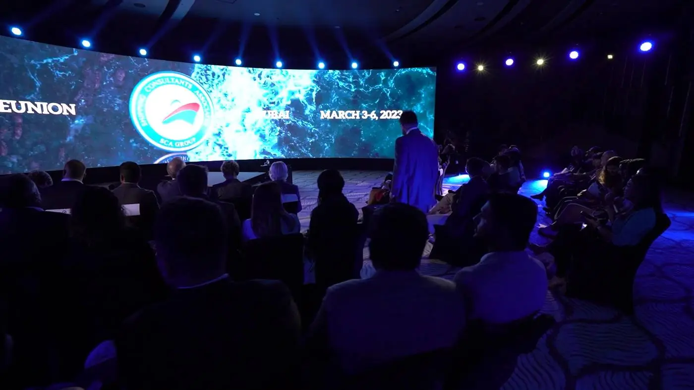 Platea al buio davanti a un ledwall curvo con il marchio della convention, a Dubai